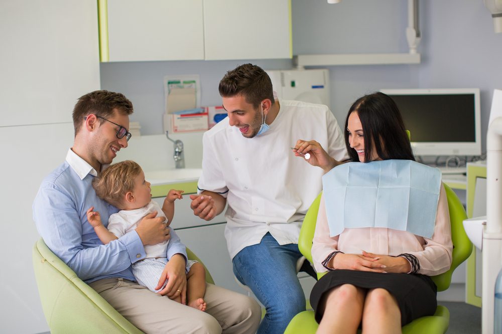 A young child in the dental chair with a parent alongside and the dentist explaining